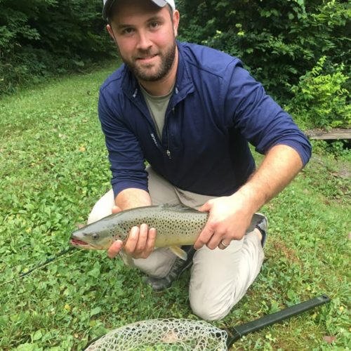 A young male fly fisherman kneeled down holding his trout.