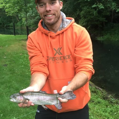 A young man in a hoody holding his trout by the stream