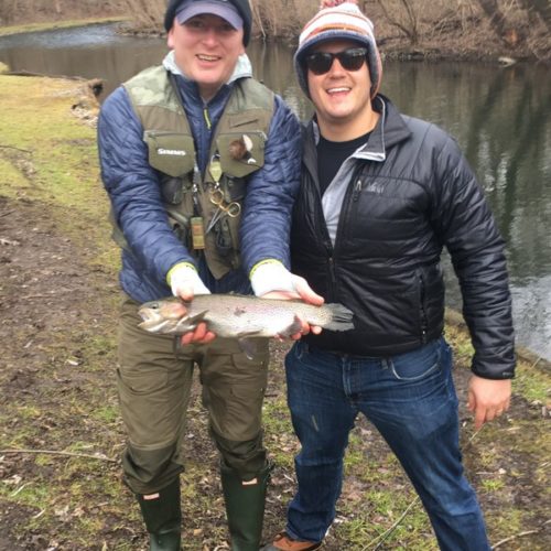 Two young male friends posing for a picture during the winter holding their trout