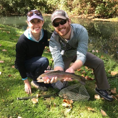 A young married couple crouched down on the bank holding their trout.