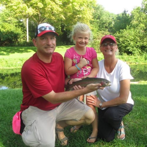A family, mom, dad and young daughter holding their trout caught at a spring creek in Ohio