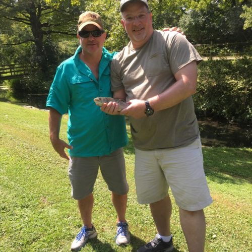 Two older gentlemen posing for a photo holding their trout.