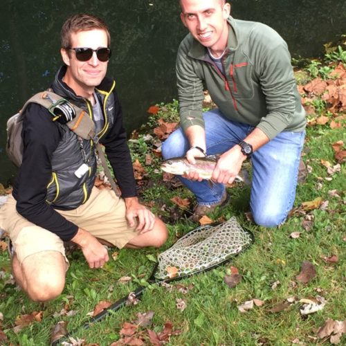 Two young men kneeled down holding fish by spring creek