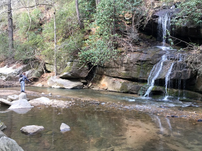 A young man casting to a pocket of water near a waterfall