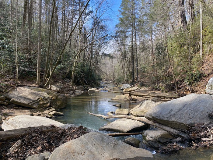 A scenic photo of the stream going down stream with big boulders in the foreground