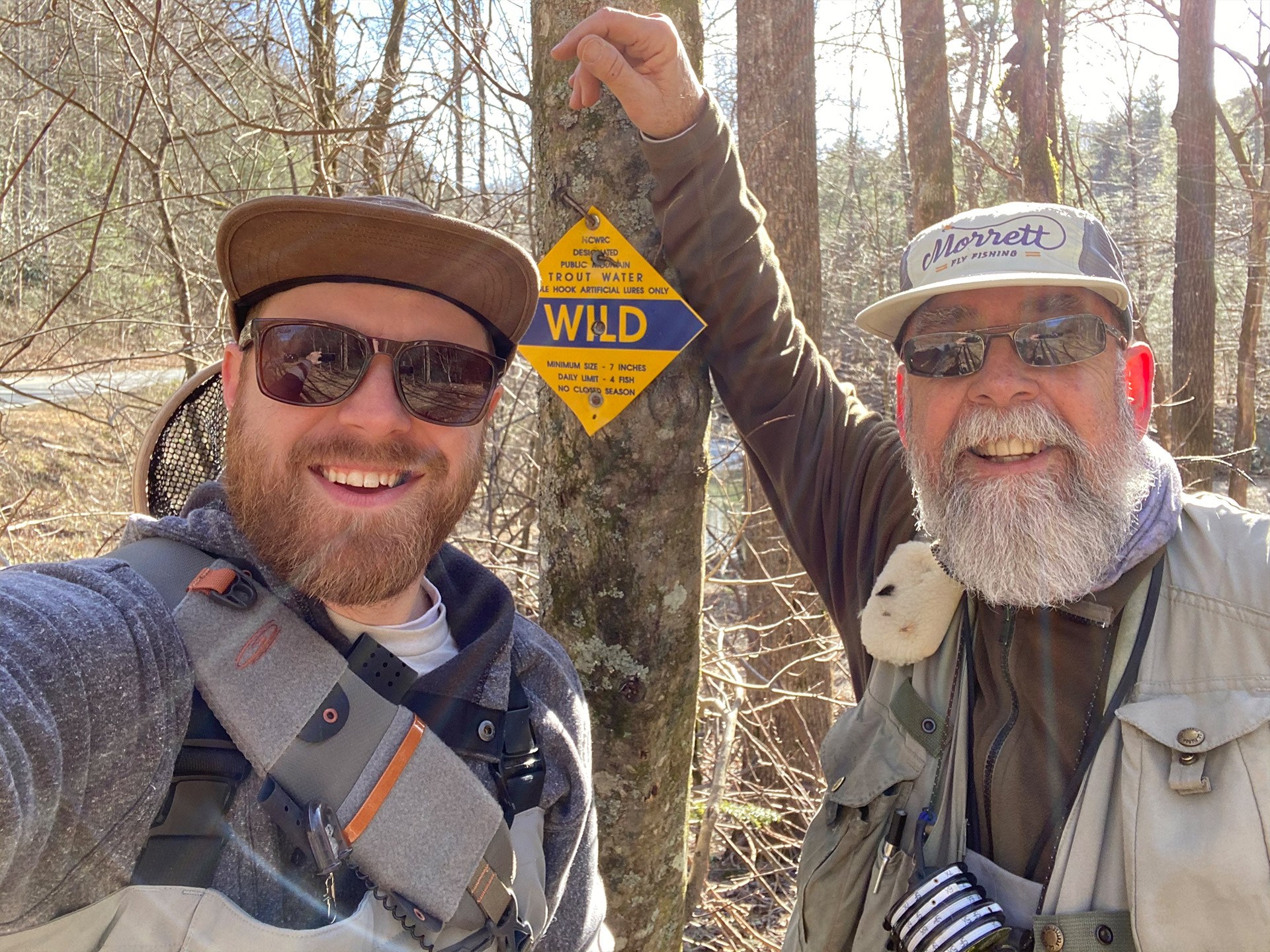 A young man in his thirties, Andy, alongside an older gentleman in his sixties, Greg, standing in front of a wild trout sign