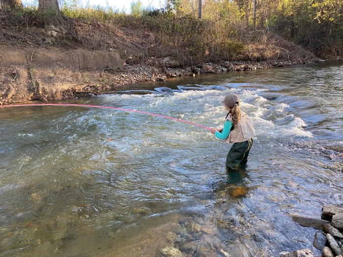 Eva wading in the stream knee-deep casting out to a stream run.