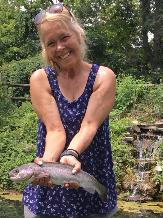 Lori standing and smiling holding her rainbow trout.