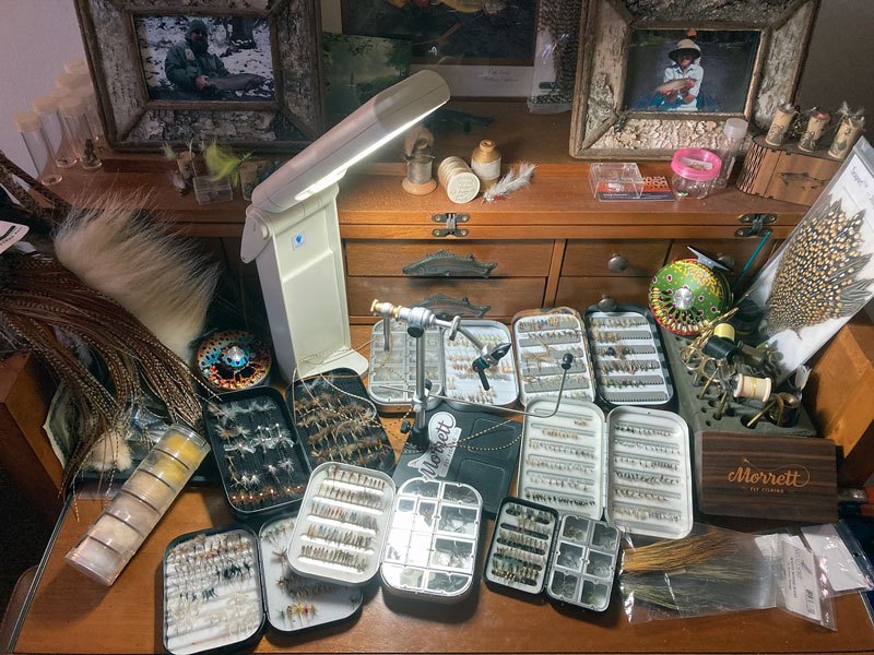 Fly boxes, materials and fly tying instruments laid out on a fly tying desk.