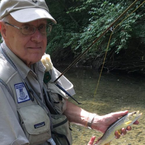 An older man standing in a river holding a brown trout