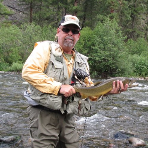 A older man standing in rock creek holding a bull trout