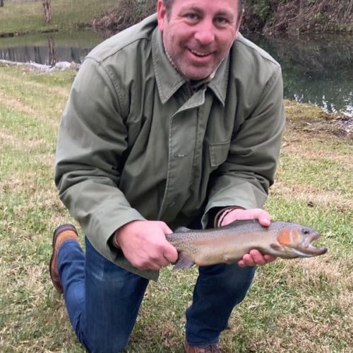 A man kneeled down holding a rainbow trout