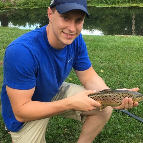 Young man crouched down holding a brown trout