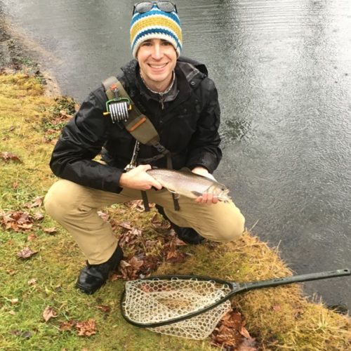 A young man crouched down while holding a brook trout