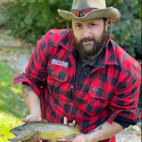 A middle-aged man wearing a flannel candidly posing with a brown trout