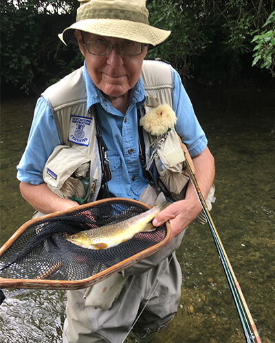 Older man holding his trout in the net with a fly vest on.